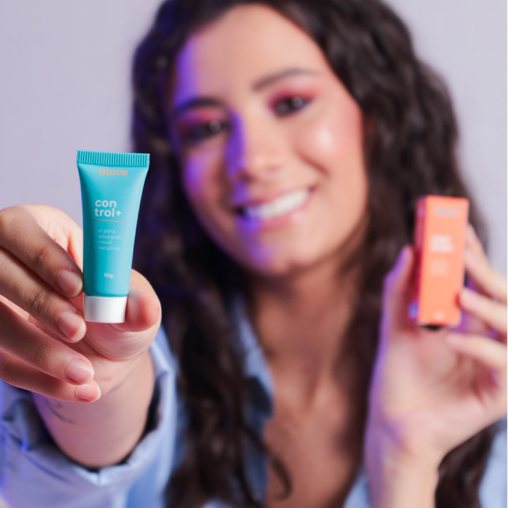 Mulher sorrindo segurando o tubo de Gel Control+ com a embalagem ao fundo