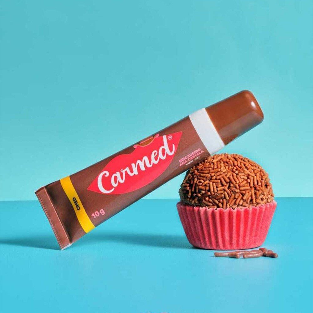 Hidratante Labial Carmed Brigadeiro com a embalagem e um doce de brigadeiro ao lado